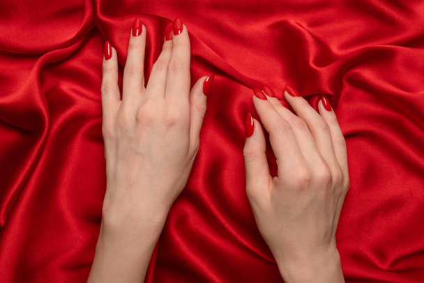 Egy vörös körmös nő keze próbálja letépni a vörös selyem szövetét..  - Fotó, kép