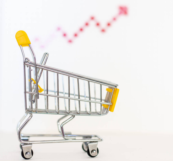 Toy shopping cart with a red growth arrow on a white background. - Фото, изображение