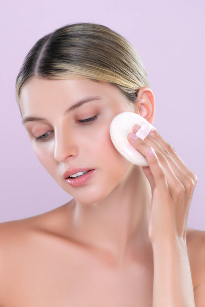 Alluring beautiful female model applying powder puff for facial makeup concept. Portrait of flawless perfect cosmetic skin woman put powder foundation on her face in pink isolated background. - Photo, Image