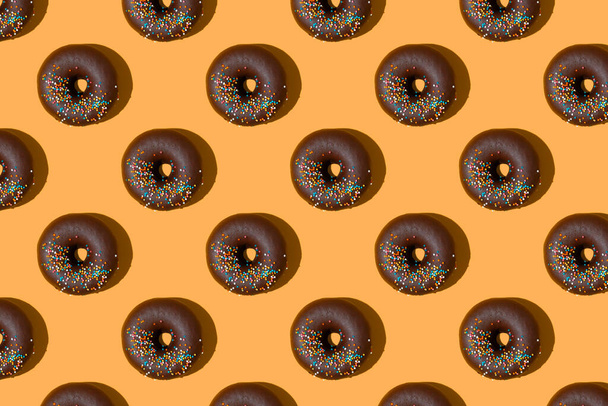 Chocolate donuts pattern isolated on orange background. Bakery, doughnut, treat, sweet food. Top view, flat lay, wallpaper, backdrop - Fotó, kép