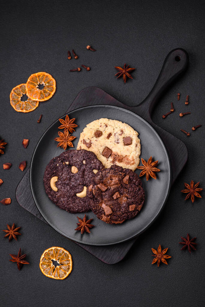 Вкусное свежее хрустящее овсяное печенье с шоколадом и орехами на черной керамической пластине на темном бетонном фоне - Фото, изображение