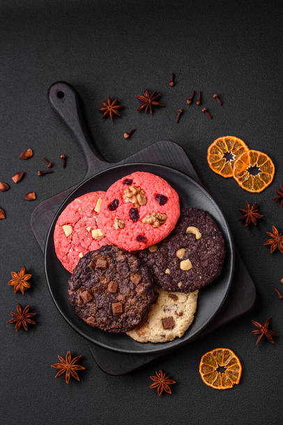 Νόστιμα φρέσκα τραγανά μπισκότα βρώμης με σοκολάτα και ξηρούς καρπούς σε μαύρο κεραμικό πιάτο σε σκούρο μπετόν φόντο - Φωτογραφία, εικόνα