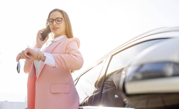 Empresaria apoyada en su coche con teléfono y llave en la mano - Foto, imagen