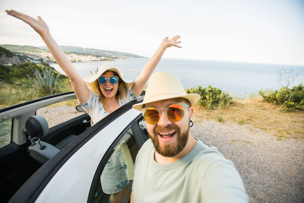 Romantic couple making selfie on smartphone camera in rental cabrio car on ocean or sea beach, enjoying summer vacation together and taking picture cellular resting near sea on weekends - Photo, Image