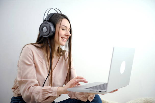 a girl with a laptop in headphones happily watches a movie listens to music studying online conference communication with friends having fun on a white background ad training course or work - Photo, Image