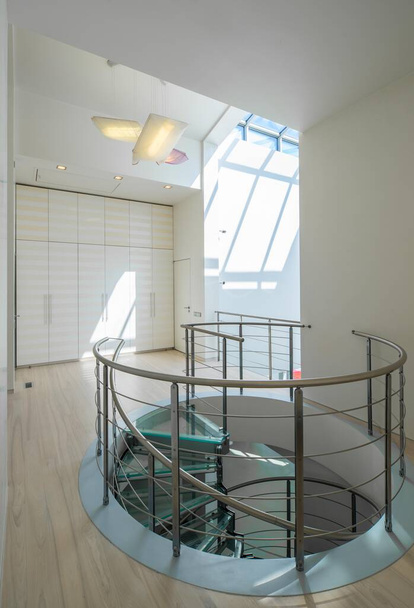 Современный интерьер зала в роскошном частном доме. Спиральная лестница из стекла и металла. Белый гардероб. - Фото, изображение