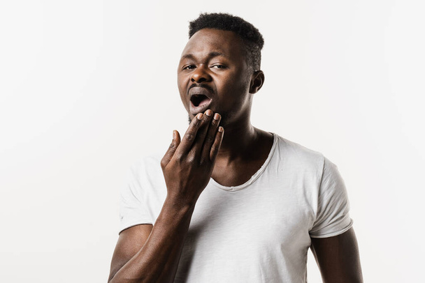 El hombre afroamericano siente dolor de muelas y molestias en los dientes. Hombre africano con caries dental, infección o lesión en el diente o encías sobre fondo blanco - Foto, imagen