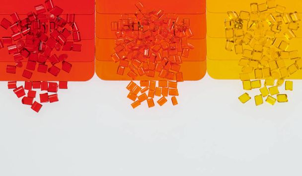 κόκκοι κόκκινης, πορτοκαλί και κίτρινης διάφανης πλαστικής ρητίνης με τις πλάκες του δείγματος χρώματος - Φωτογραφία, εικόνα