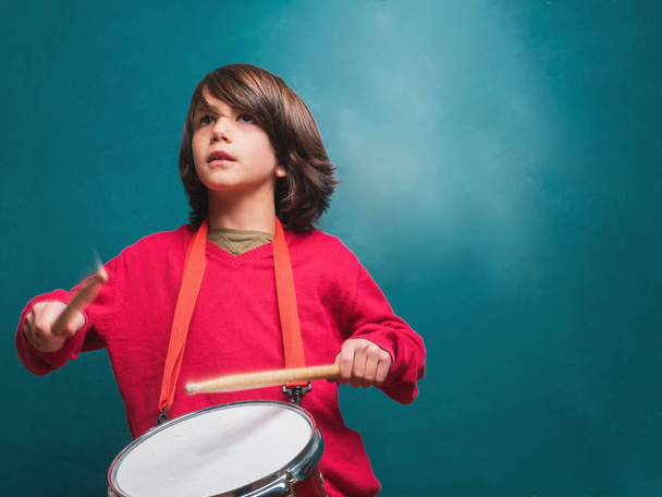 赤いセーターを着た男の子が学校の黒板の前で太鼓を演奏 - 写真・画像
