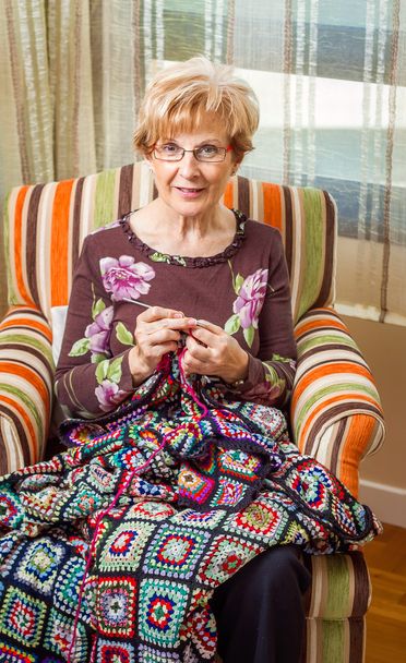 Mujer mayor tejiendo un edredón de lana con parches
 - Foto, Imagen