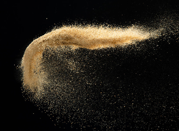 Sand flying explosion, Golden sand wave explode. Abstract sands cloud fly. Yellow colored sand splash throwing in Air. Black background Isolated high speed shutter, throwing freeze stop motion - Foto, Bild
