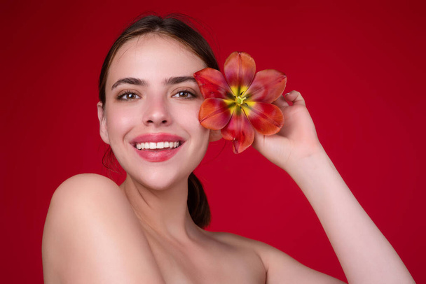 Youth and skin care concept. Beauty girl with tulip near face. Beautiful sensual woman hold tulips, studio portrait on red background - Fotoğraf, Görsel