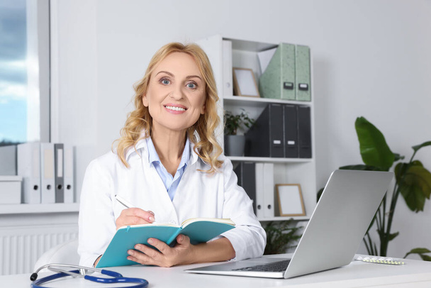 Doctor with laptop and notebook at desk in clinic. Online medicine concept - Fotoğraf, Görsel