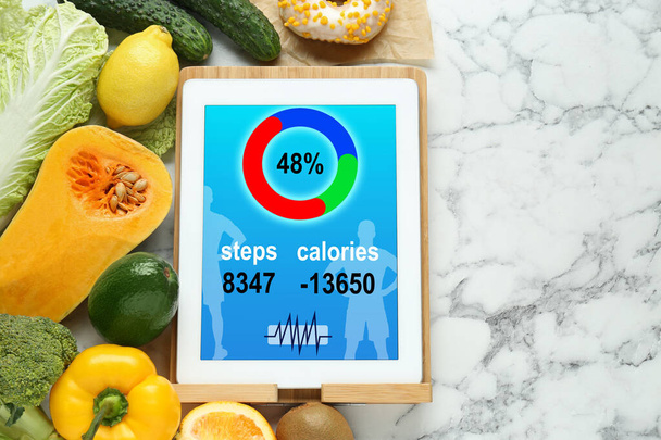 Tablet with weight loss calculator application and food products on white marble table, flat lay. Space for text - Valokuva, kuva