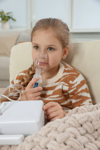 Little girl using nebulizer for inhalation in armchair at home - Foto, imagen