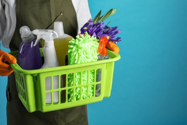 Spring cleaning. Woman holding basket with detergents, flowers and tools on light blue background, closeup. Space for text - Photo, image