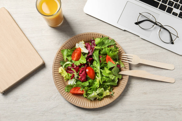 Fresh vegetable salad, glass of juice and laptop on white wooden table at workplace, flat lay. Business lunch - Foto, afbeelding