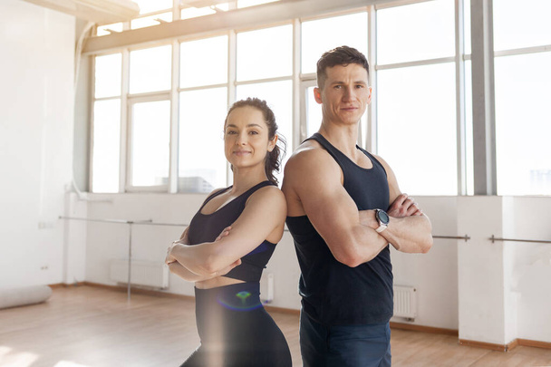 beautiful athletic couple in sportswear stands in the gym in the morning, fitness girl and coach man in training in bright room - Foto, afbeelding
