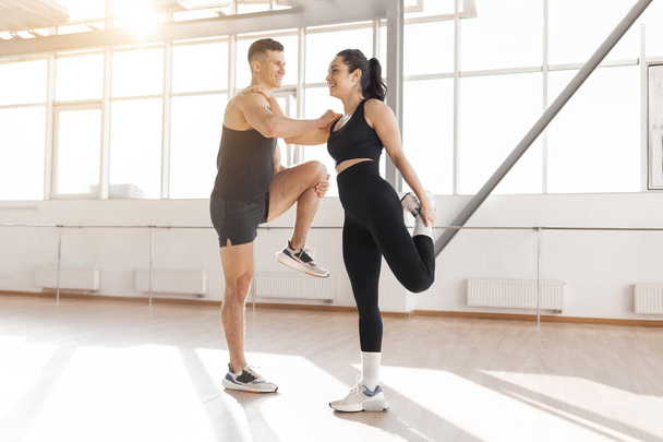 beautiful athletic couple in sportswear warm up in the gym in the morning, fitness girl and coach man go in for sports in training in bright room - Photo, Image