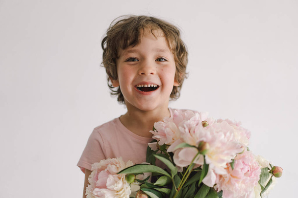 Cheerful happy child with Peonys bouquet. Smiling little boy on white background. Mothers Day. Love and romantic concept - Φωτογραφία, εικόνα