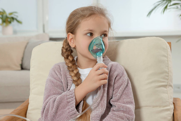 Little girl using nebulizer for inhalation in armchair at home - Foto, Imagen
