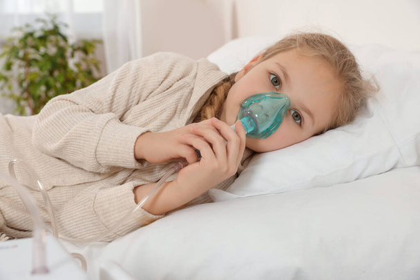 Little girl using nebulizer for inhalation on bed at home - Fotoğraf, Görsel