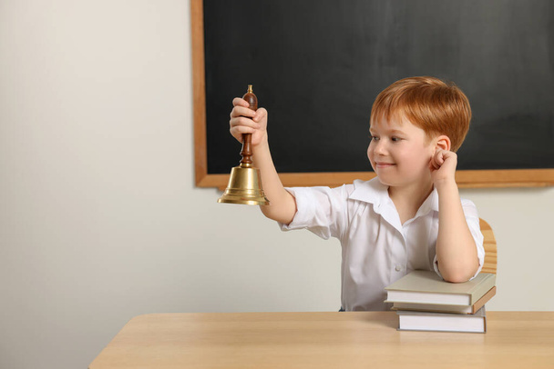 Cute little boy ringing school bell in classroom, space for text - Fotografie, Obrázek