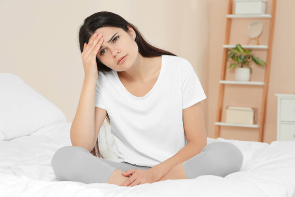 Young woman suffering from headache on bed at home. Hormonal disorders - Foto, imagen