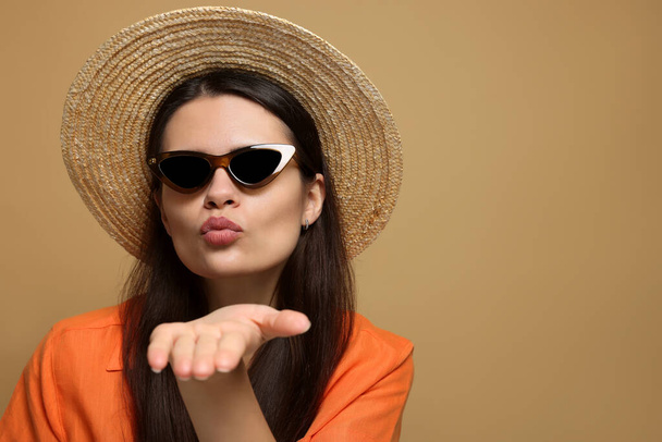 Beautiful young woman in straw hat blowing kiss on beige background. Space for text - Foto, imagen