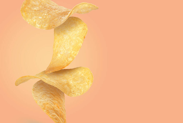 Stack of tasty potato chips on pale coral background, space for text - Zdjęcie, obraz