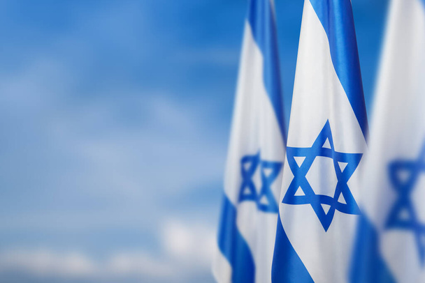 Israel flags with a star of David over cloudy sky background. Patriotic concept about Israel with national state symbols. Banner with place for text. - Fotografie, Obrázek