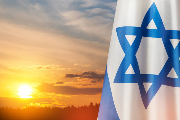 Israel flag with a star of David over cloudy sky background on sunset. Patriotic concept about Israel with national state symbols. Banner with place for text. - Zdjęcie, obraz