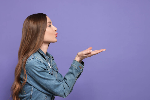 Beautiful young woman blowing kiss on purple background, space for text - Fotó, kép