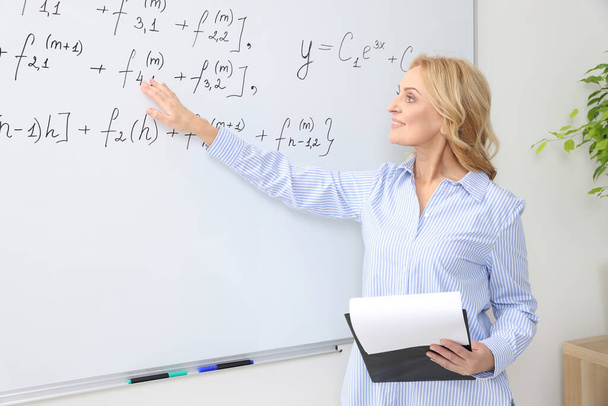 Professor with clipboard giving lecture near whiteboard in classroom - Φωτογραφία, εικόνα
