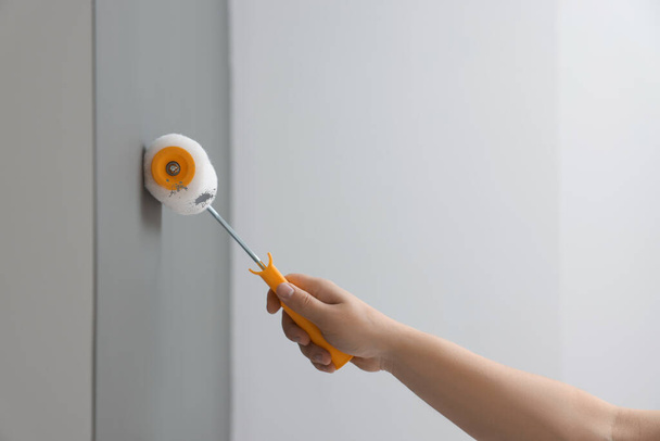 Worker using roller to paint wall with grey dye indoors, closeup - 写真・画像