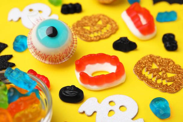 Tasty colorful jelly candies and Halloween decorations on yellow background, closeup - Foto, immagini