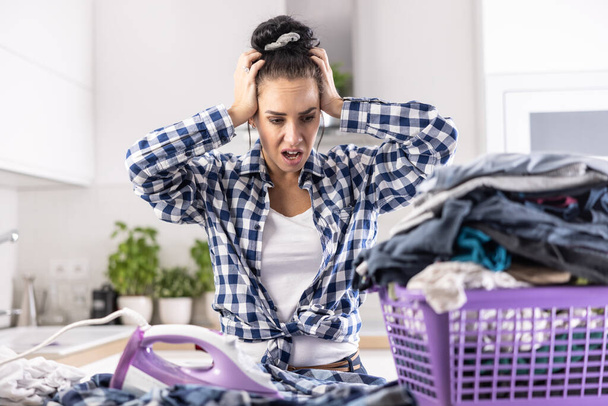 Housewife has shocked expression and mouth open over neverending chores and basket full of unironed clothes. - Foto, Bild