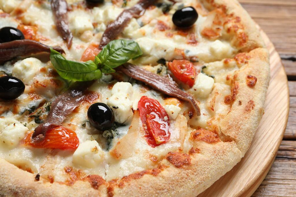 Tasty pizza with anchovies, basil and olives on wooden table, closeup - 写真・画像