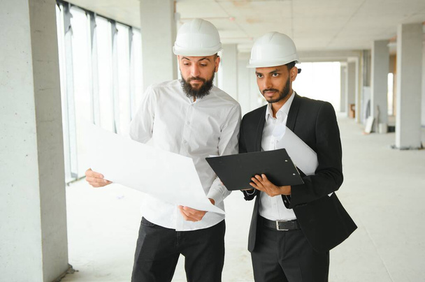 Multiracial male coworkers in hardhats discussing project on construction site. - Foto, imagen