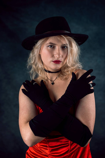 hermosa mujer joven usar vestido rojo elegante y sombrero negro aislado sobre fondo oscuro. Concepto de vida - Foto, imagen