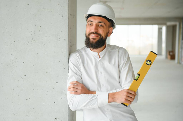 Portrait of good-looking Middle Eastern guy wearing safety helmet and holding construction plan. Employees and business concept - Φωτογραφία, εικόνα