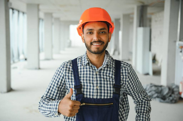Indian male construction worker standing in uniform and hard hat at construction site - Foto, Bild