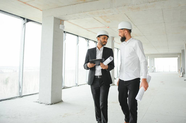 Multiracial male coworkers in hardhats discussing project on construction site. - Φωτογραφία, εικόνα
