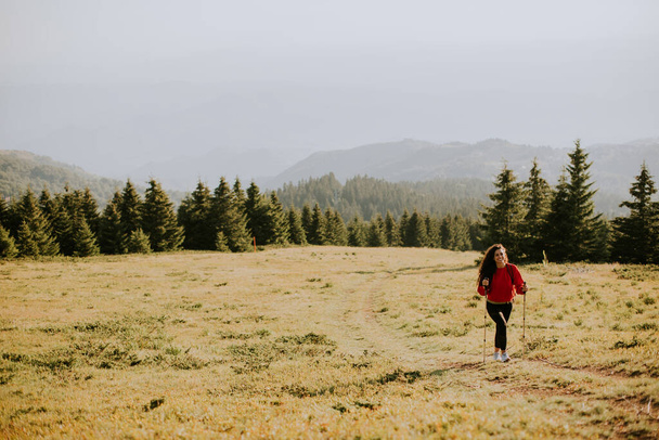 Giovane donna sorridente che cammina con lo zaino sulle colline verdi - Foto, immagini