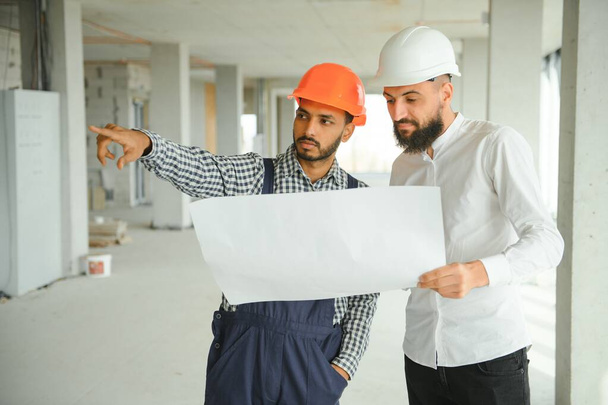 Multiracial male coworkers in hardhats discussing project on construction site. - Foto, afbeelding