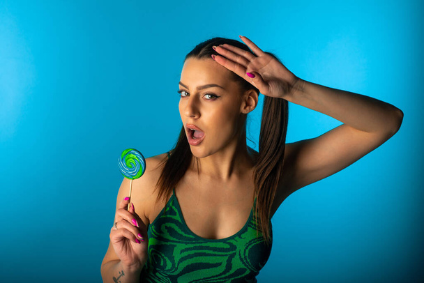 Cute girl posing with green lollipop  on a blue backround in the studio - Fotoğraf, Görsel