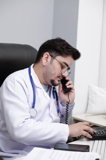 Ein junger Arzt sitzt in der Klinik und telefoniert. - Foto, Bild