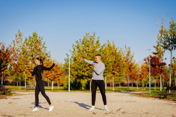 Gorgeous girl and good looking man, a couple, warming up their bodies before workout in the park - Fotografie, Obrázek