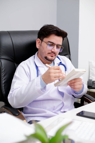 Een jonge arts zit in de kliniek dagboek te lezen en houdt pen in de hand. - Foto, afbeelding