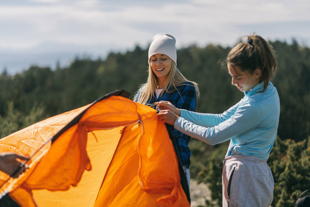 Zwei Freunde lächeln und basteln das orangefarbene Zelt, während sie am Berg stehen - Foto, Bild
